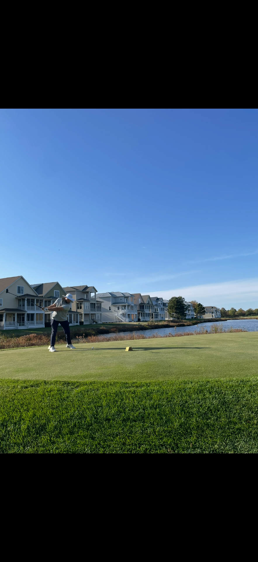 Golfer teeing off near a waterfront fairway